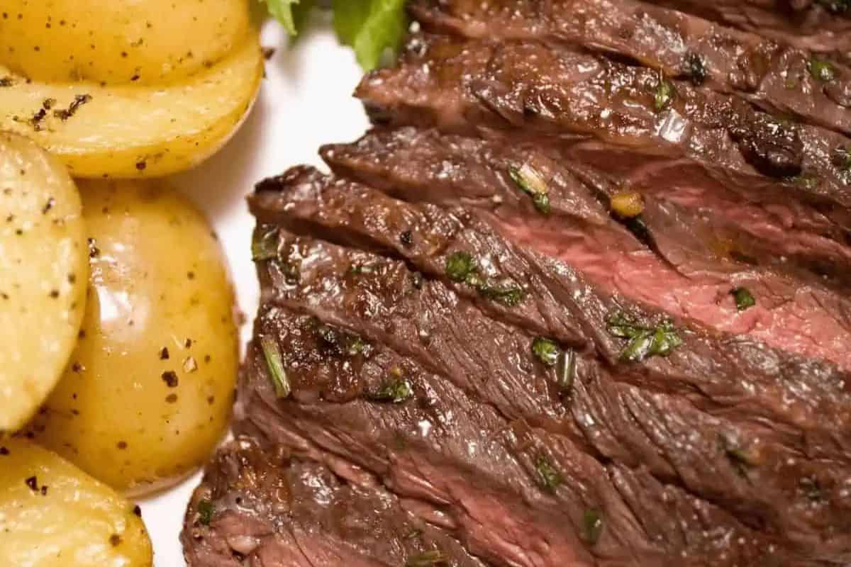 Sliced juicy steak with herbs next to seasoned roasted potatoes on a white plate—a steakhouse classic perfect for trying new steak recipes.