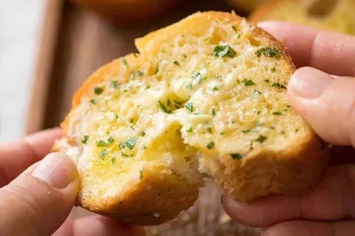 Close-up of a piece of garlic bread, topped with a sprinkle of cheese and parsley flakes.