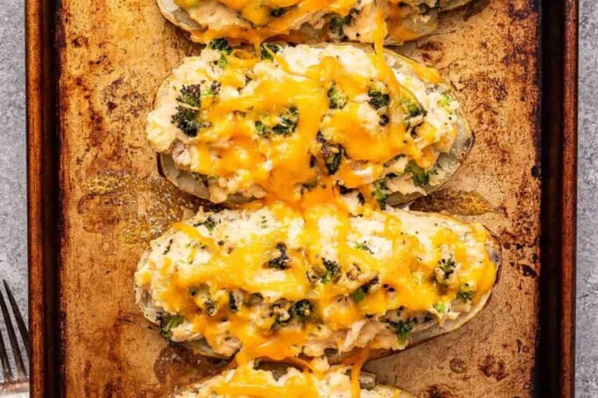 Three twice-baked potatoes topped with broccoli, shredded cheese, and a creamy chicken filling on a baking sheet—perfect inspiration for your next baked potato recipes.