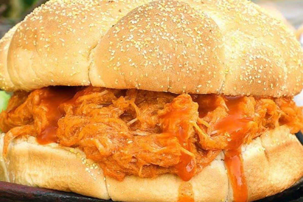 Close-up of a sandwich with a sesame seed bun filled with shredded canned chicken, barbecue sauce, and a drizzle of sauce—perfect for budget friendly dinners and easy dinner recipes.