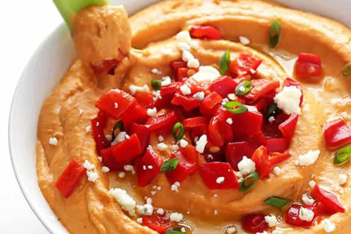 Bowl of classic hummus topped with chopped red peppers, green onions, and crumbled cheese—a fresh twist on traditional hummus recipes.