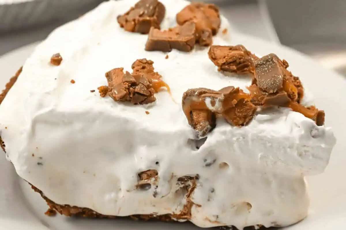 A slice of pie with a thick layer of whipped topping and pieces of chocolate and caramel candy scattered on top—perfect for fans of easy pie recipes.
