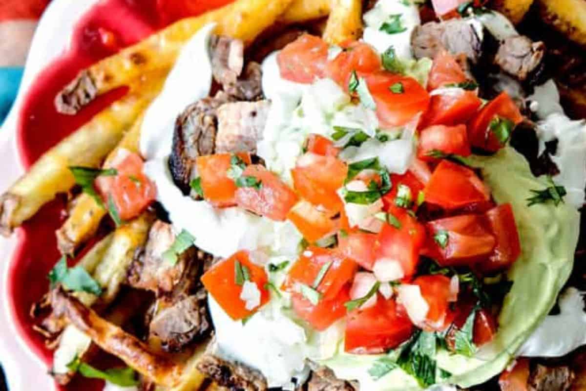 A plate of fries topped with grilled steak, sour cream, chopped tomatoes, onions, and cilantro makes for one of those crazy good French fry recipes packed with flavor in every bite.