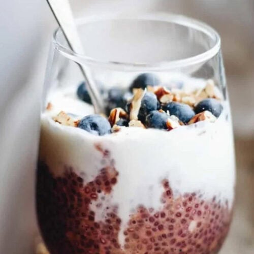 A glass filled with chia pudding, topped with yogurt, fresh blueberries, chopped nuts, and a spoon—perfect for morning meals or as inspiration for easy breakfast and overnight oats recipes.
