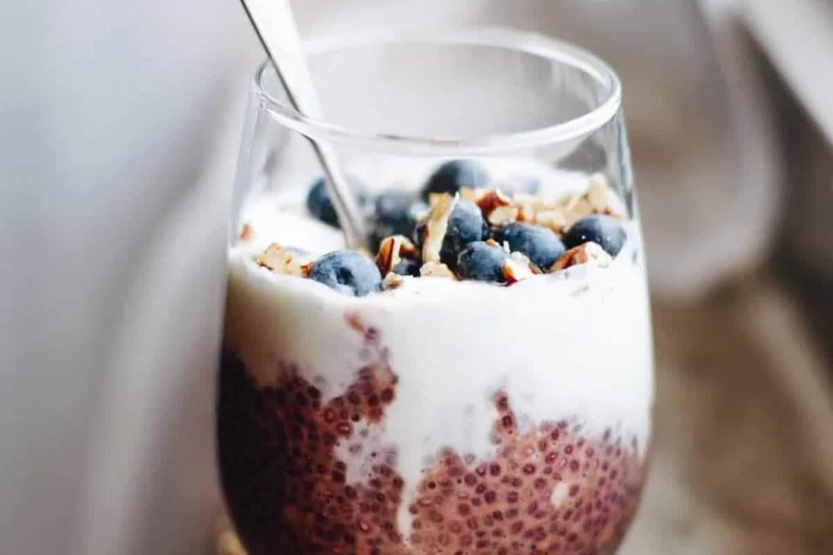A glass filled with chia pudding, topped with yogurt, fresh blueberries, chopped nuts, and a spoon—perfect for morning meals or as inspiration for easy breakfast and overnight oats recipes.
