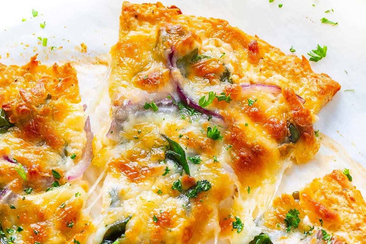 Close-up of cheesy chicken crust pizza slices topped with red onions, green herbs, and melted cheese—an ideal option for cheap meals and budget friendly dinners.
