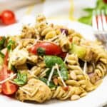 A plate of Chicken and Pesto Pasta Salad with rotini, grilled chicken, spinach, cherry tomatoes, red onions, pine nuts, and shredded cheese.