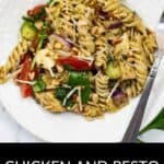 A plate of Chicken and Pesto Pasta Salad with rotini, tomatoes, zucchini, red onion, cheese, pine nuts, and a fork on the side.