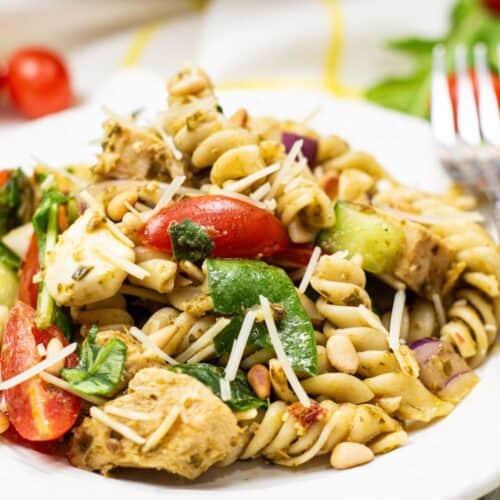 A plate with rotini, grilled chicken, spinach, cherry tomatoes, red onion, pine nuts, and shredded cheese.