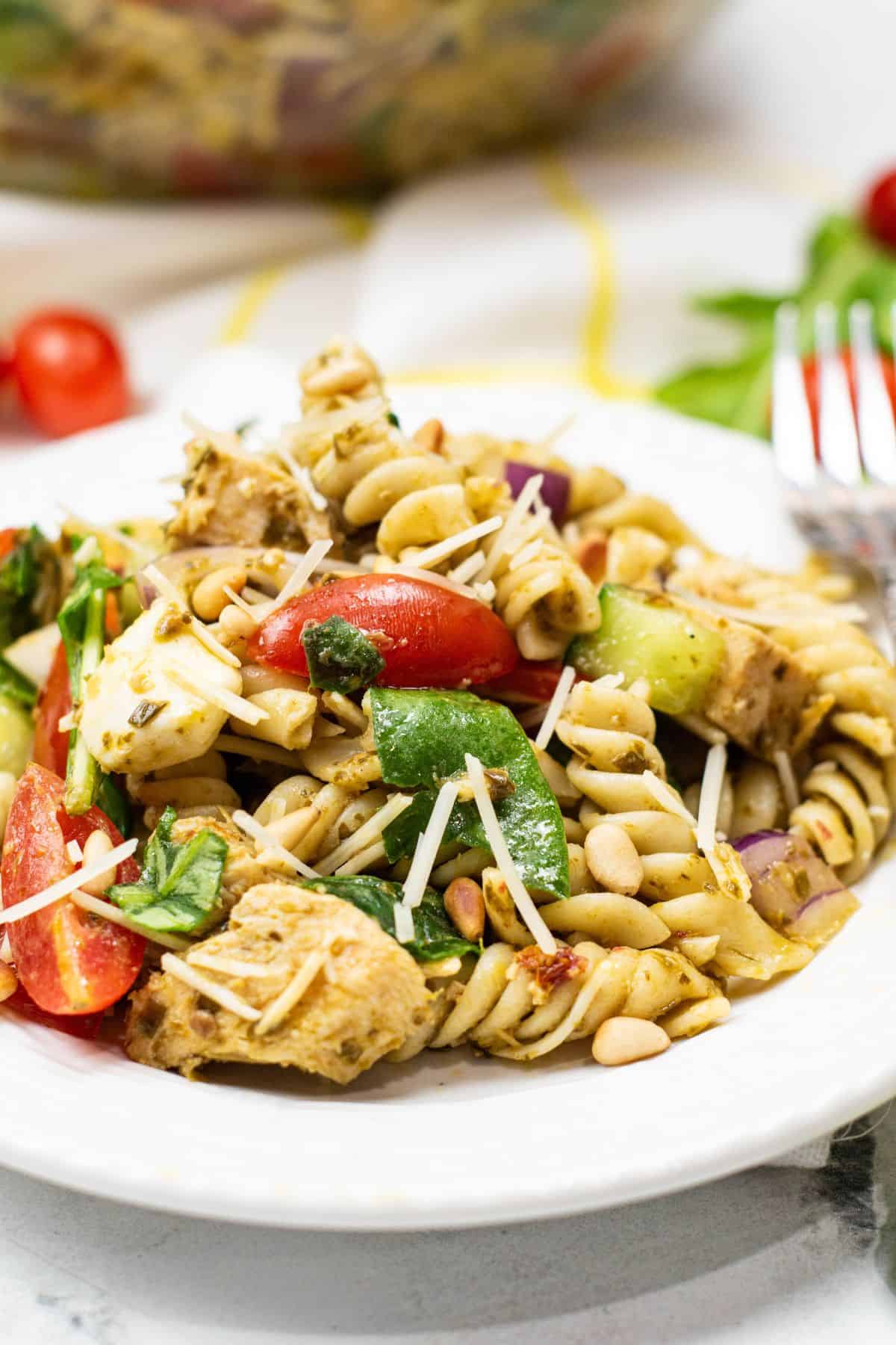 A plate with rotini, grilled chicken, spinach, cherry tomatoes, red onion, pine nuts, and shredded cheese.