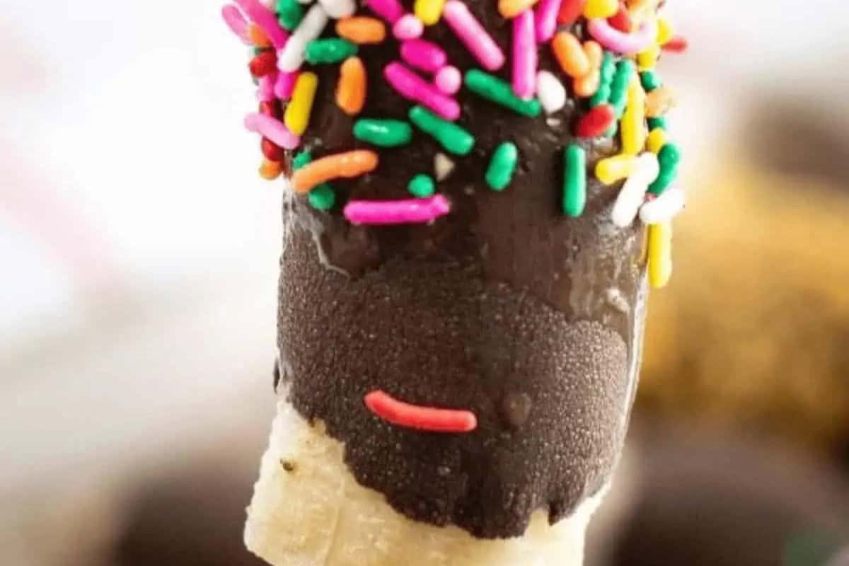A close-up of a banana piece dipped in chocolate and covered with multicolored sprinkles—an irresistible dessert that's perfect for summer treats.