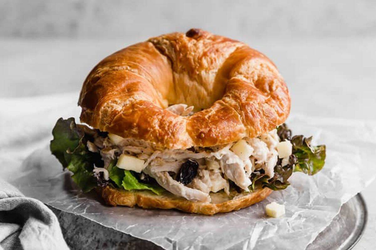 A croissant sandwich filled with chicken salad made from canned chicken, lettuce, and diced cheese sits on crumpled parchment paper—a perfect pick for easy dinners.