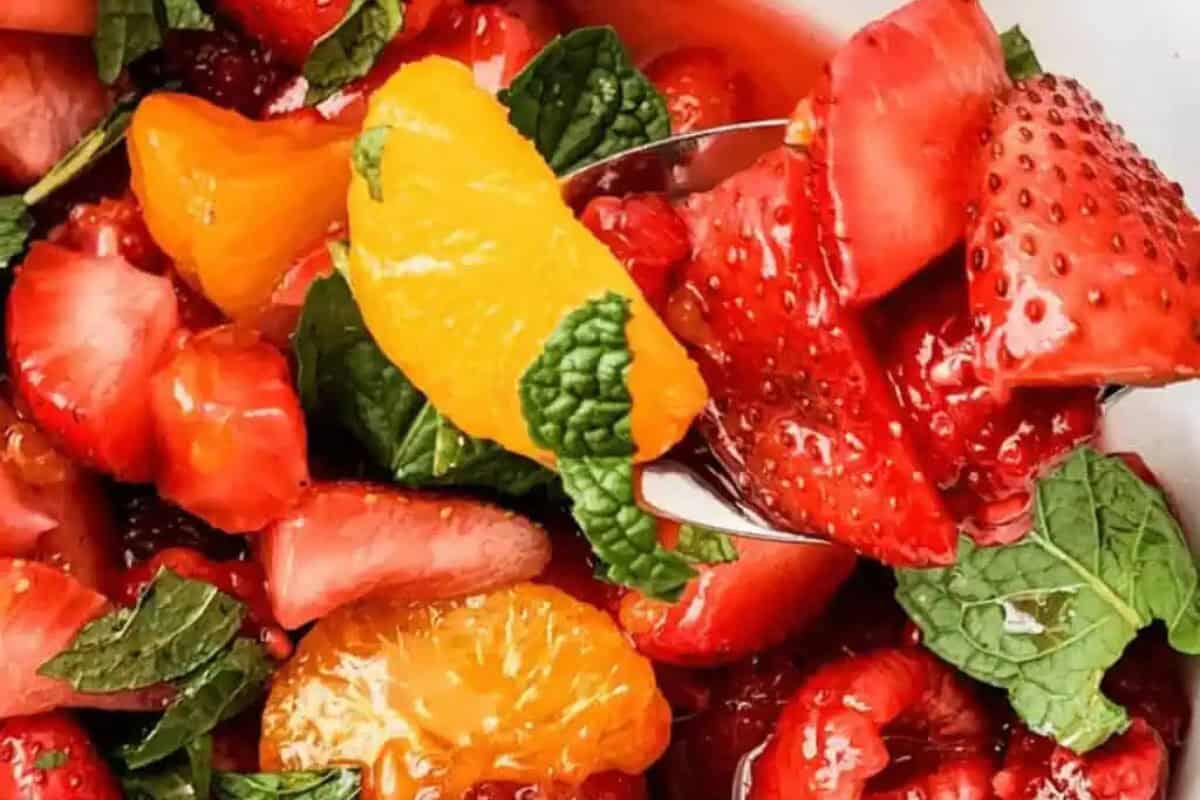 Close-up of a beautiful fruit salad with sliced strawberries, mandarin orange segments, raspberries, and fresh mint leaves—perfect inspiration for your own delicious fruit salads.