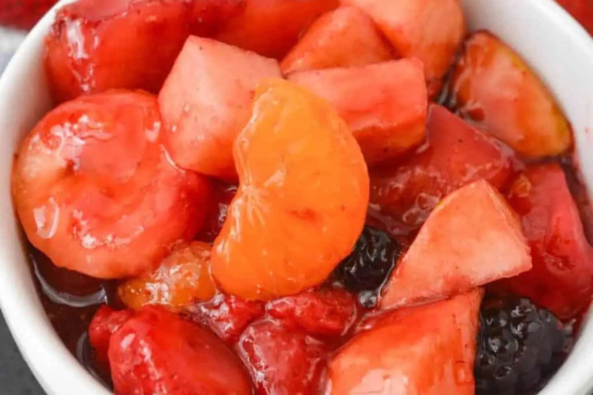 A bowl filled with mixed fruit, including mandarin orange segments, apple pieces, strawberries, and berries in syrup—perfect inspiration for delicious fruit salads and creative fruit salad recipes.