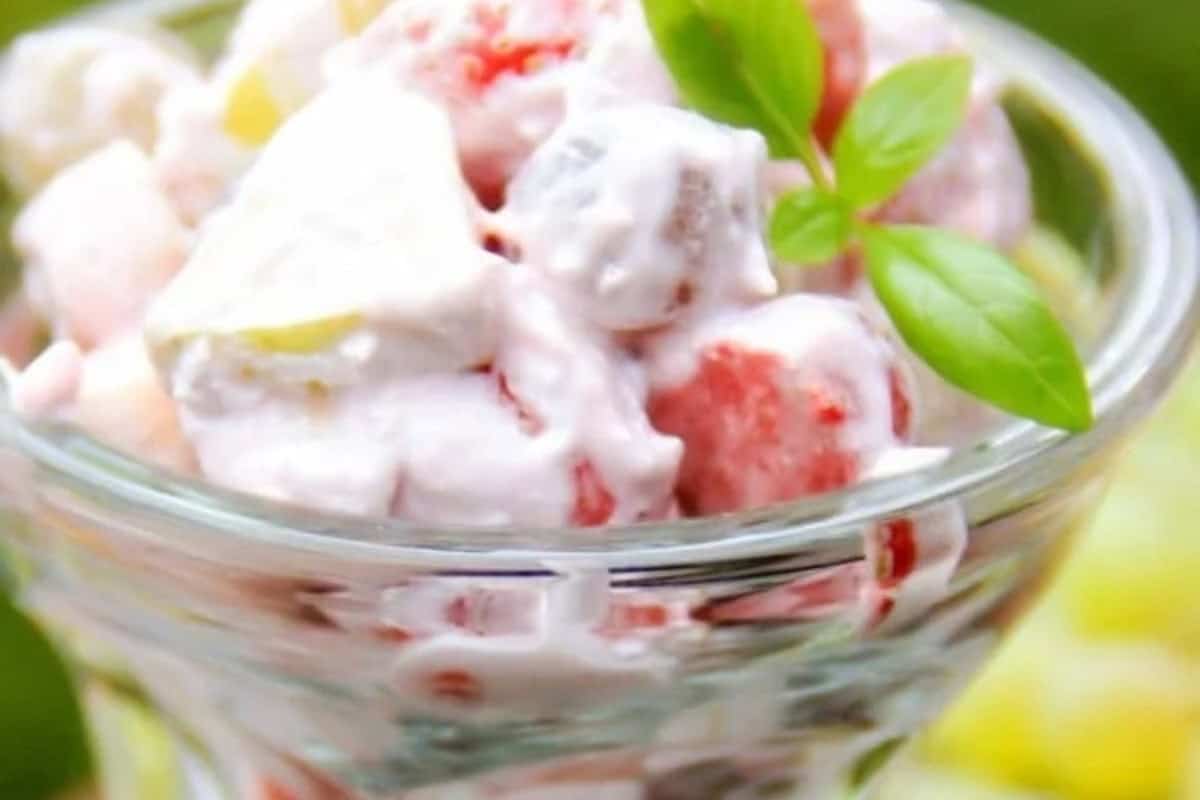 A glass bowl filled with creamy fruit salad, garnished with a small sprig of fresh green basil—a perfect example of beautiful fruit salads.