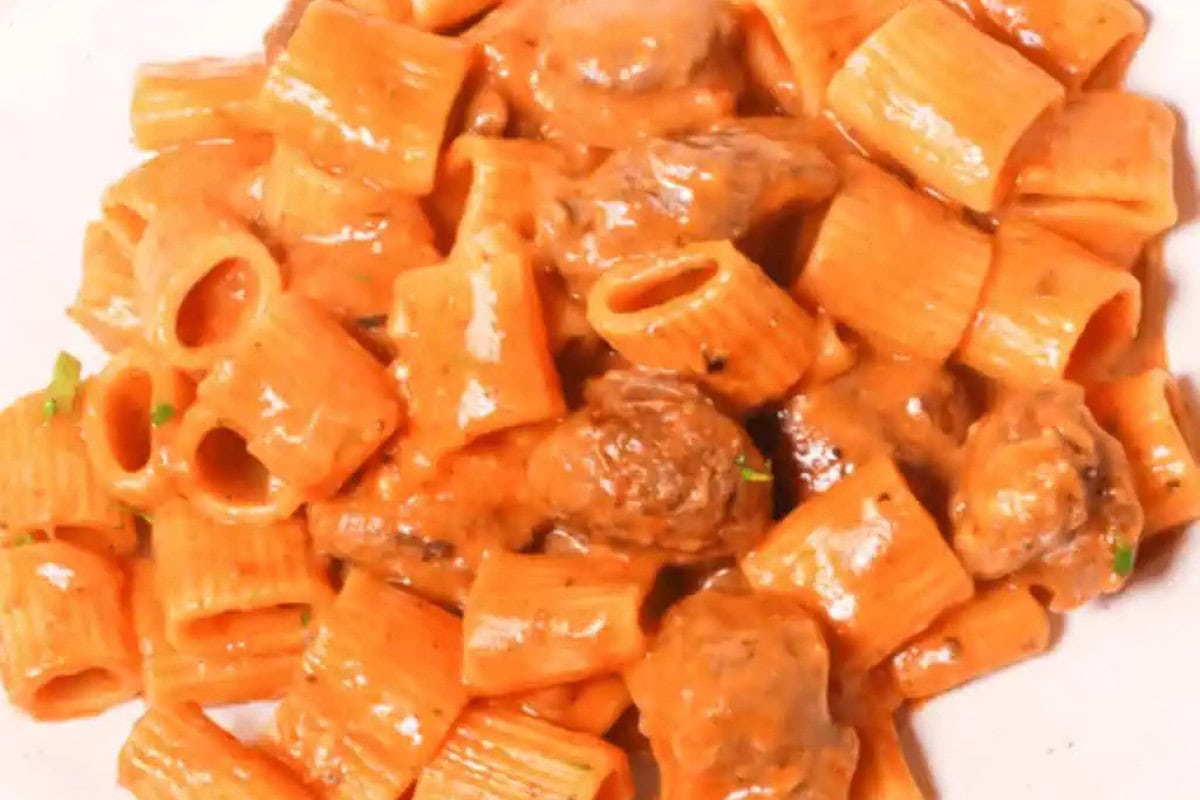 Close-up of rigatoni pasta with meatballs, coated in a creamy tomato sauce, served on a white plate—just like Nonna’s recipes.