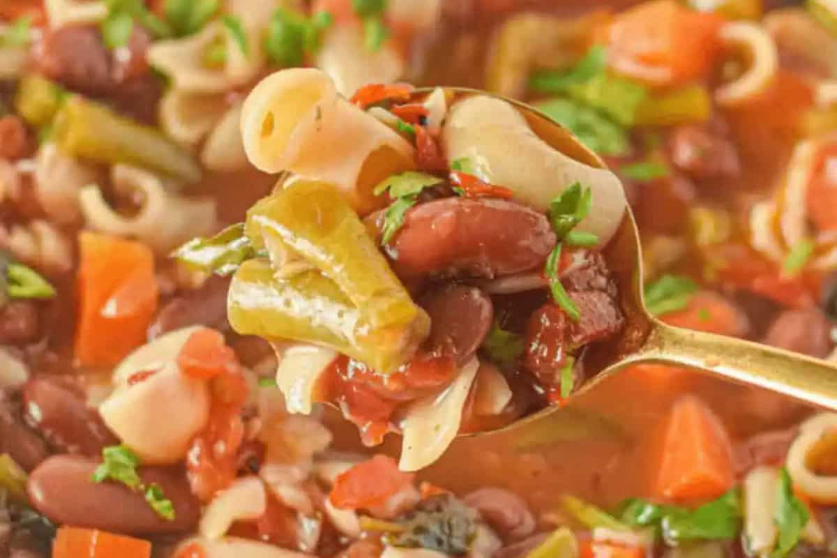 A close-up of a spoonful of vegetable soup with pasta, beans, green beans, carrots, tomatoes, and chopped herbs—just like Nonna’s recipes for classic homemade Italian soups.