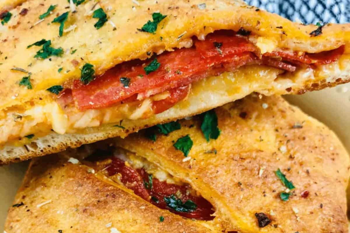 Close-up of two golden-brown calzones filled with melted cheese and pepperoni, garnished with chopped parsley—a delicious nod to classic homemade Italian recipes.
