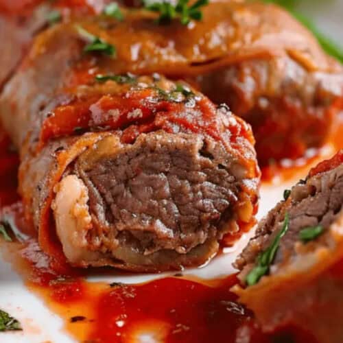 Sliced braciole topped with tomato sauce, showing rolled beef and herbs on a white plate with basil garnish—a classic favorite from Nonna’s recipes.