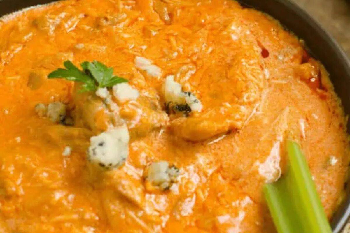 Close-up of a bowl of cottage cheese buffalo chicken dip, topped with blue cheese crumbles and a piece of celery.