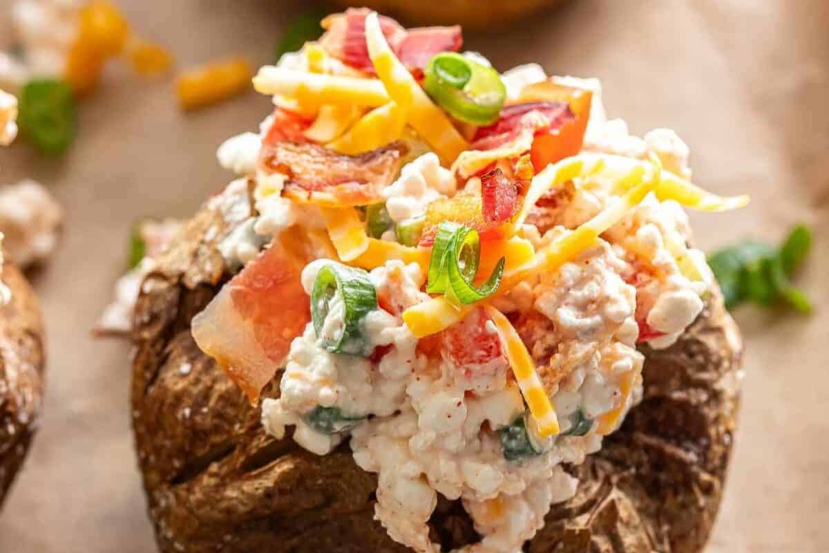 A creative baked potato topped with cottage cheese, shredded cheddar cheese, chopped tomatoes, green onions, and bacon pieces—perfect for those looking for new baked potato ideas.