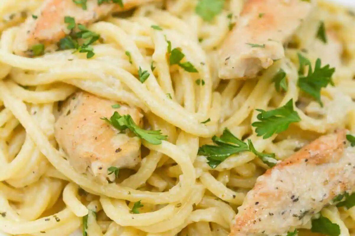 A close-up of creamy spaghetti pasta with pieces of cooked chicken, garnished with chopped parsley and a swirl of bold pesto for an extra burst of flavor.