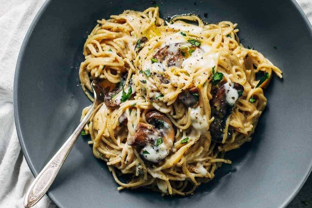 A plate of creamy pasta with mushrooms, garnished with herbs and black pepper, served with a fork—this is a must try for fans of delicious mushroom dishes.