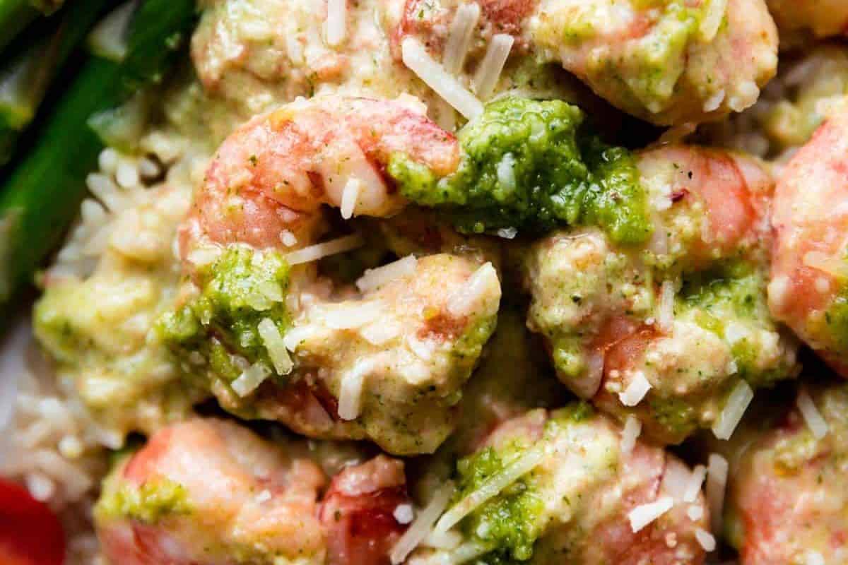 Close-up of cooked shrimp topped with bold pesto sauce and grated cheese.