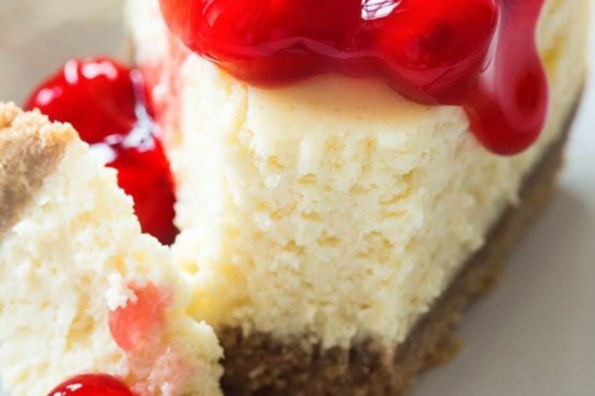 A slice of cheesecake with a graham cracker crust, topped with cherry sauce and whole cherries—a perfect treat for fans of effortless desserts.