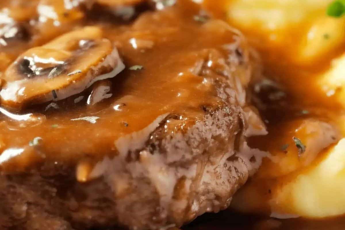 Close-up of a juicy steak with brown mushroom gravy, served alongside creamy mashed potatoes—a classic steakhouse favorite.
