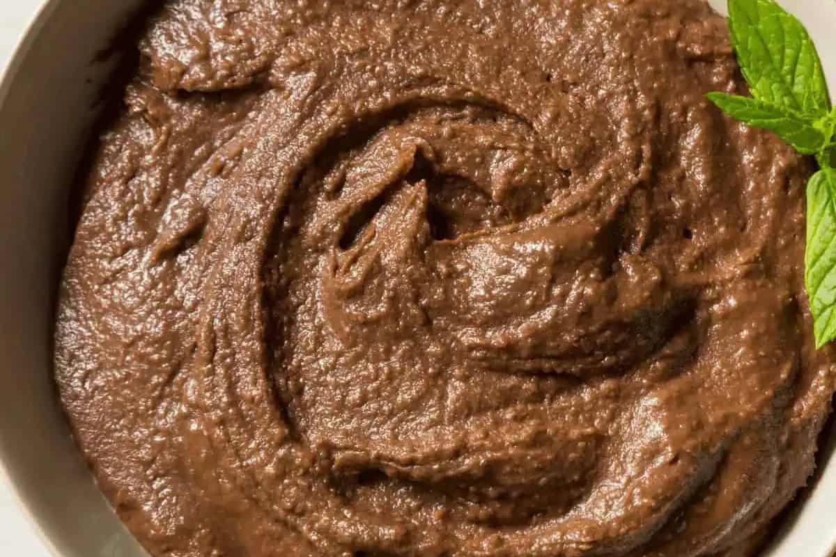 A close-up of thick, swirled chocolate spread or mousse in a white bowl with a small sprig of mint on the side, offering delicious twists to classic hummus-inspired desserts.