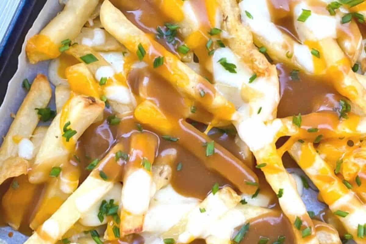 Flavorful fries topped with melted cheese, rich brown gravy, and chopped chives on a baking tray—these crazy good fries are a must-try for fans of indulgent French fry recipes.