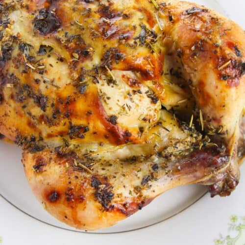 Dutch Oven Roasted Chicken seasoned with herbs and spices, served on a white plate with a green floral border.