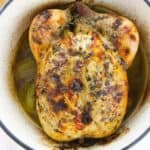 Roasted with herbs and browned skin sits in a white pot surrounded by savory juices and tender cooked onions.