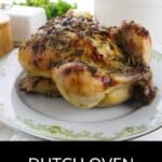 A whole Dutch Oven Roasted Chicken with herbs is served on a decorative plate, with a white Dutch oven and greenery in the background. Text reads: "Dutch Oven Roasted Chicken.