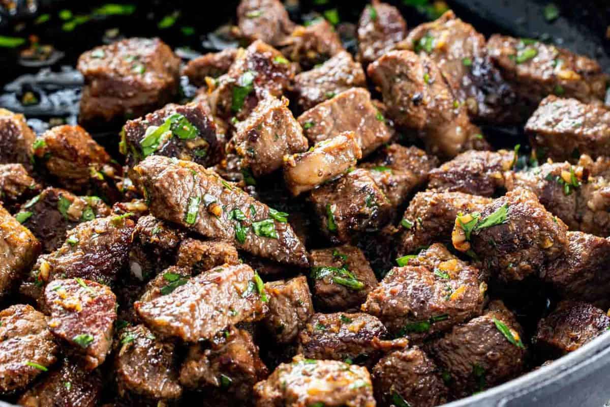 Juicy steak cubes garnished with chopped herbs and seasonings, shown close up in a pan—perfect inspiration for your next steakhouse dinner or delicious steak recipes at home.