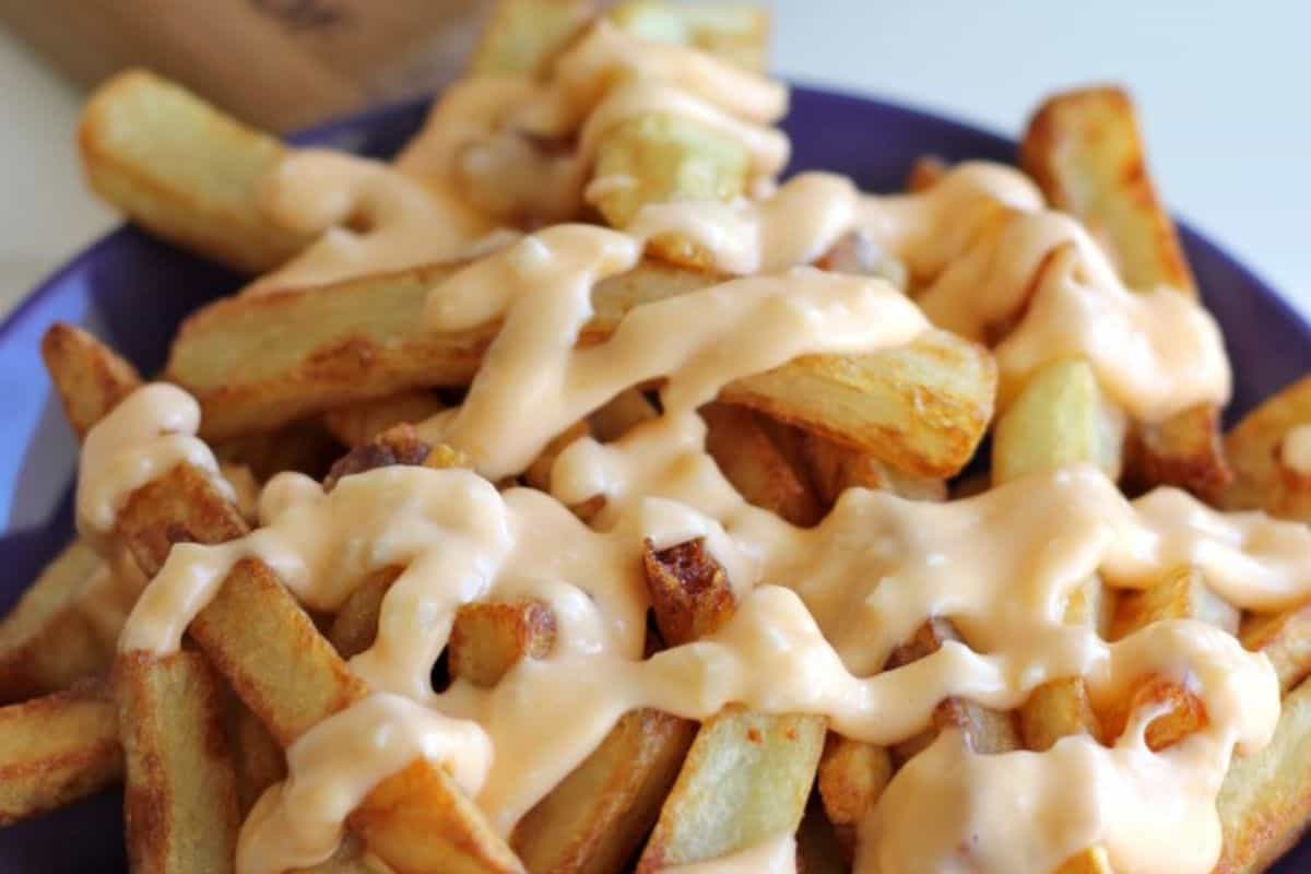 A plate of thick-cut French fries topped with a generous drizzle of creamy, light orange sauce delivers crazy good flavor in every bite.
