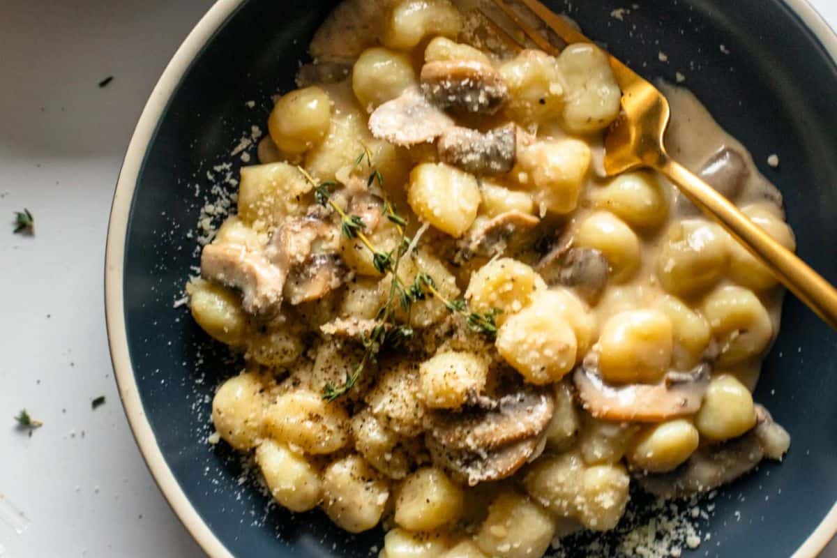 A plate of gnocchi with creamy mushroom sauce, garnished with fresh thyme and grated cheese, with a gold fork resting on the side—this is a must try for lovers of mushroom dishes beyond the basics.