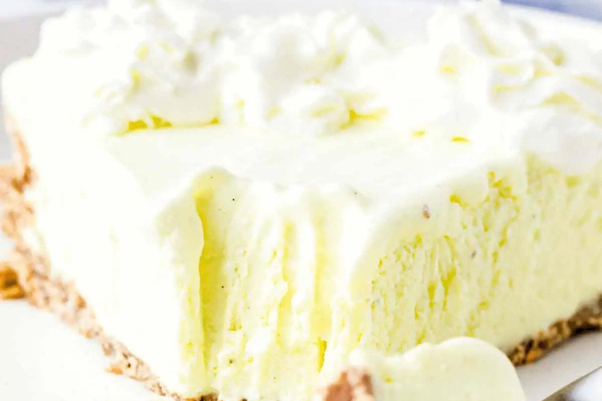 A close-up of a slice of creamy lemon pie with a graham cracker crust and whipped cream topping on a white plate—a perfect choice for fans of irresistible summer desserts.