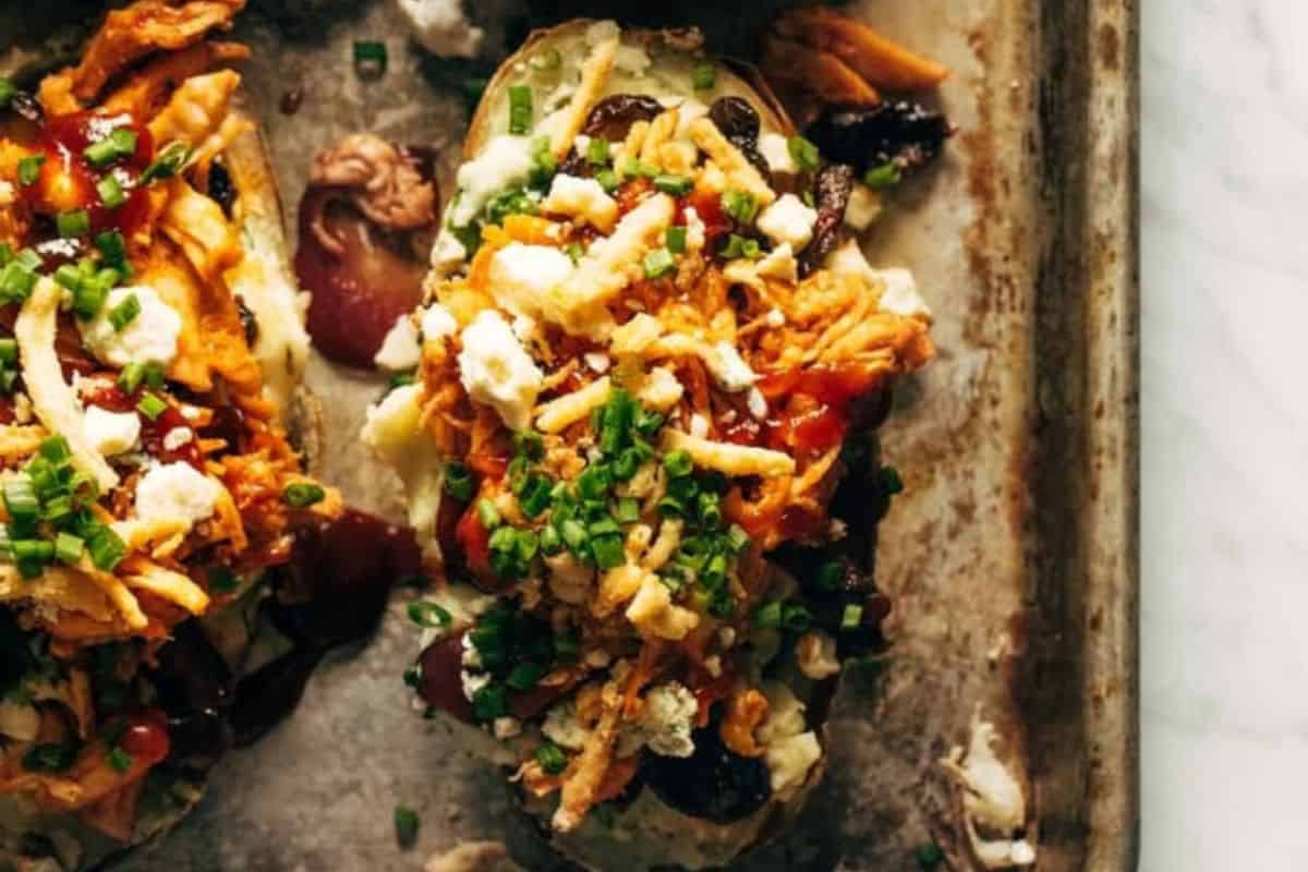 A delicious baked potato topped with shredded meat, crispy fried onions, cheese, barbecue sauce, and chives—a perfect choice for those seeking creative baked potato ideas or new potato recipes.