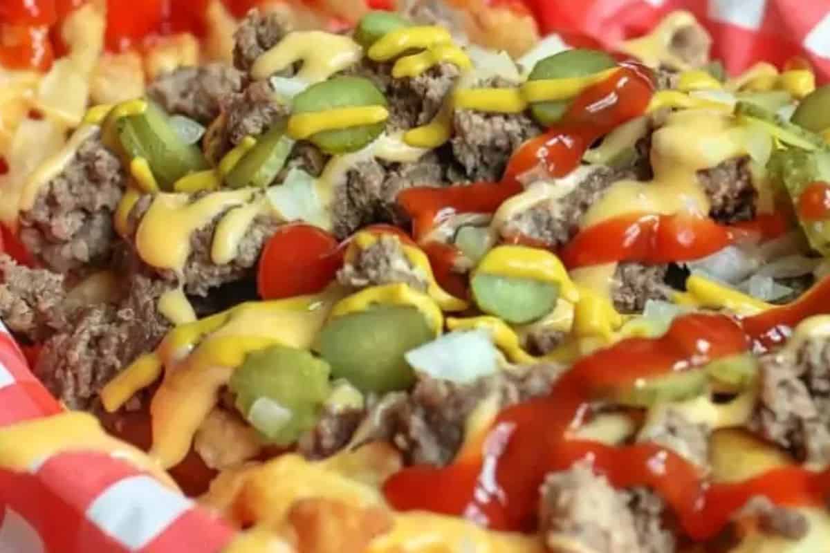 A close-up of crazy good crinkle-cut fries topped with ground beef, sliced pickles, diced onions, ketchup, and melted cheese brings bold flavor to a red-and-white checkered tray—one of the best French fry recipes you’ll try.