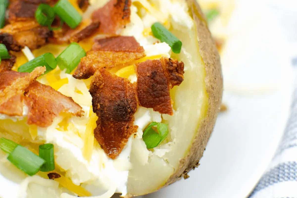 A baked potato topped with sour cream, shredded cheese, crispy bacon pieces, and chopped green onions—a delicious twist for those seeking creative baked potato ideas.