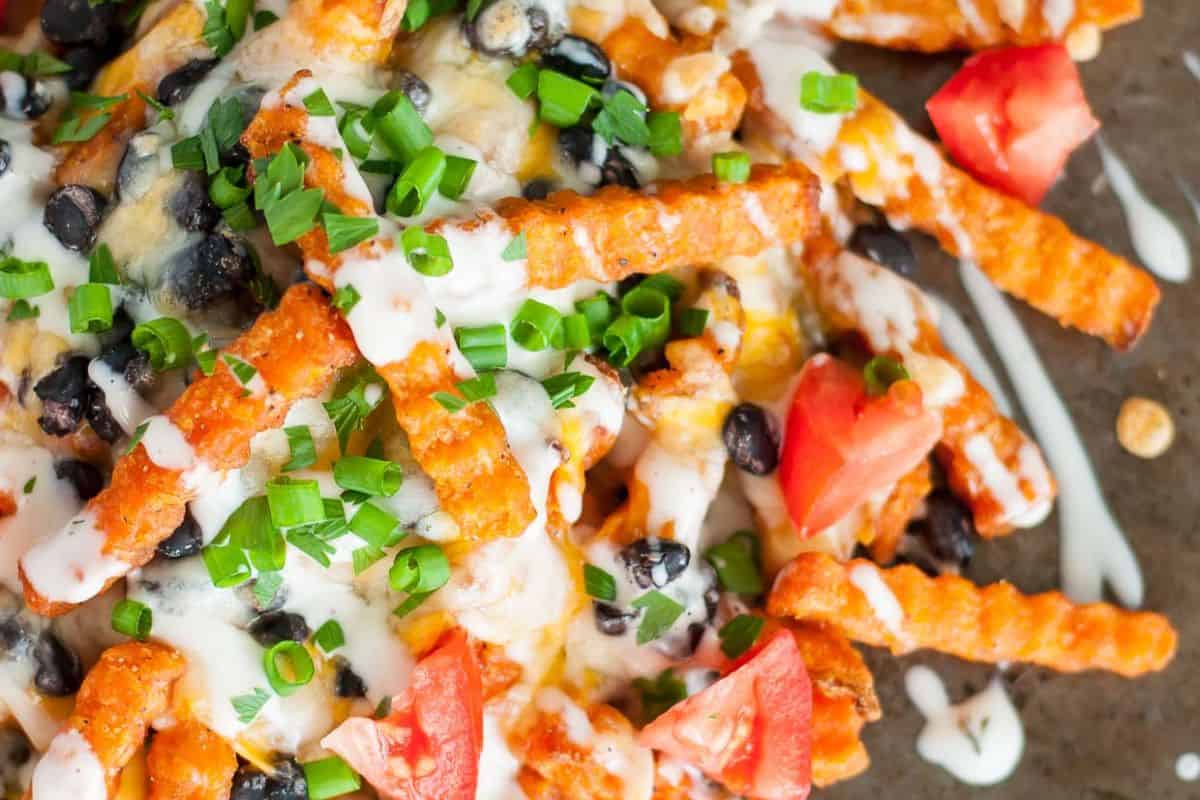 Crinkle-cut sweet potato fries topped with black beans, melted cheese, diced tomatoes, chopped green onions, and drizzled with white sauce deliver crazy good flavor—a must-try for fans of bold French fry recipes.