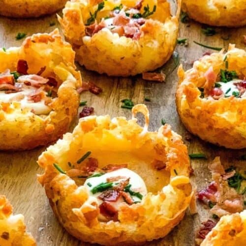 Crispy potato nests filled with sour cream, bacon bits, and chopped chives make for delicious cold appetizer ideas, beautifully arranged on a wooden surface.