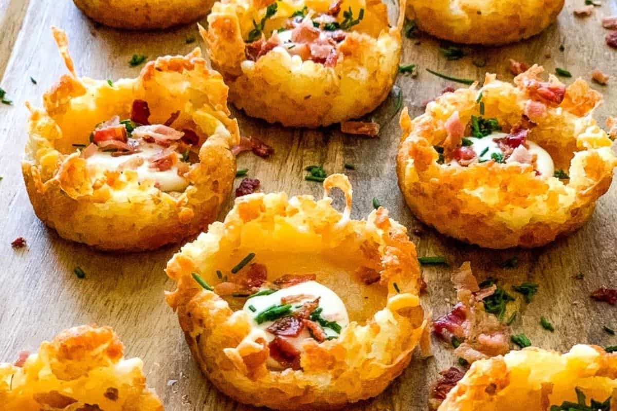 Crispy potato nests filled with sour cream, bacon bits, and chopped chives make for delicious cold appetizer ideas, beautifully arranged on a wooden surface.