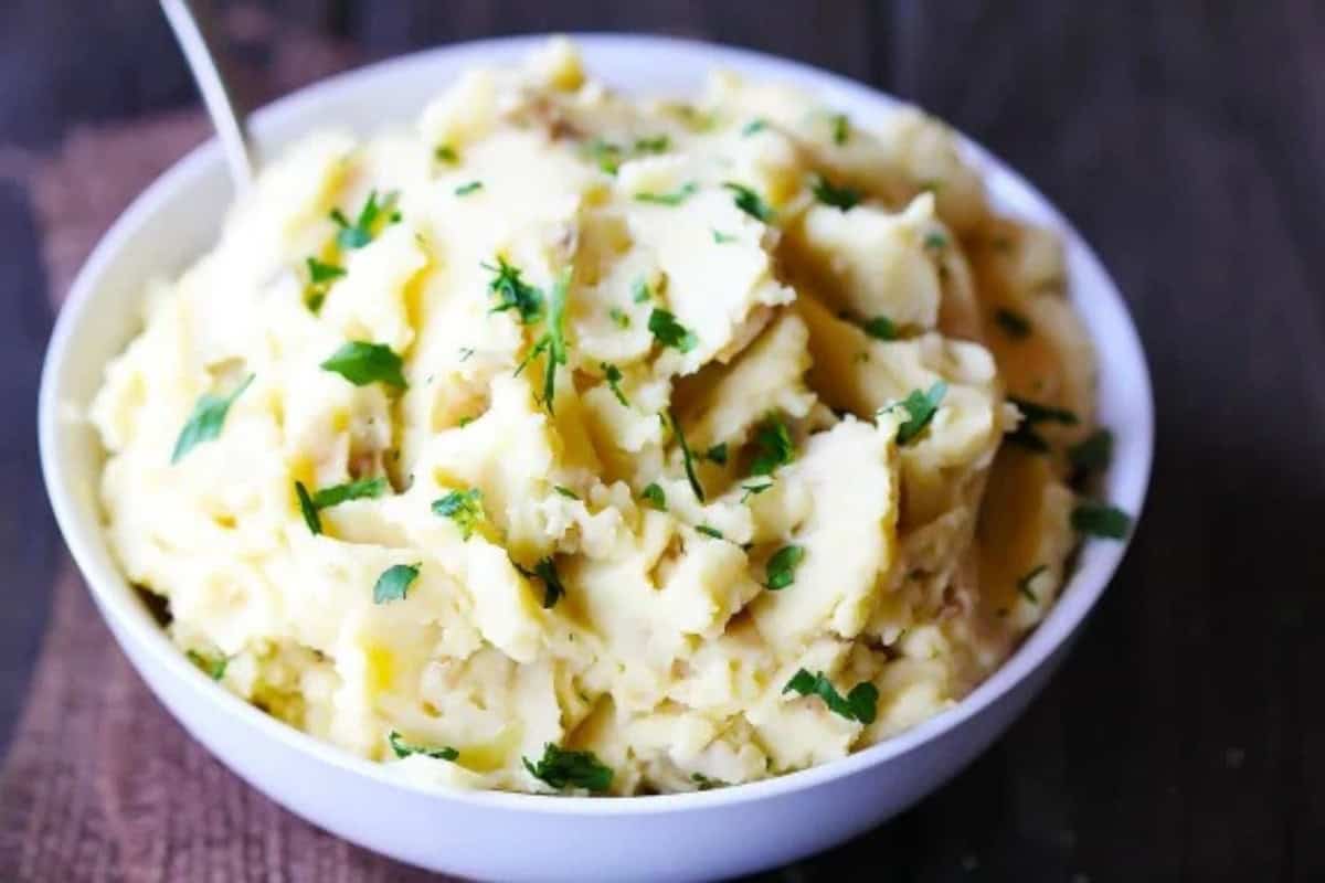 A white bowl filled with mashed potatoes, garnished with chopped fresh parsley, sits on a dark wooden surface—perfect for those craving delicious twists or seeking inspiration for creative hummus recipes.