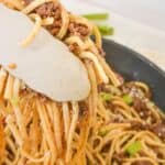 Tongs grabbing a serving of the pasta dish.