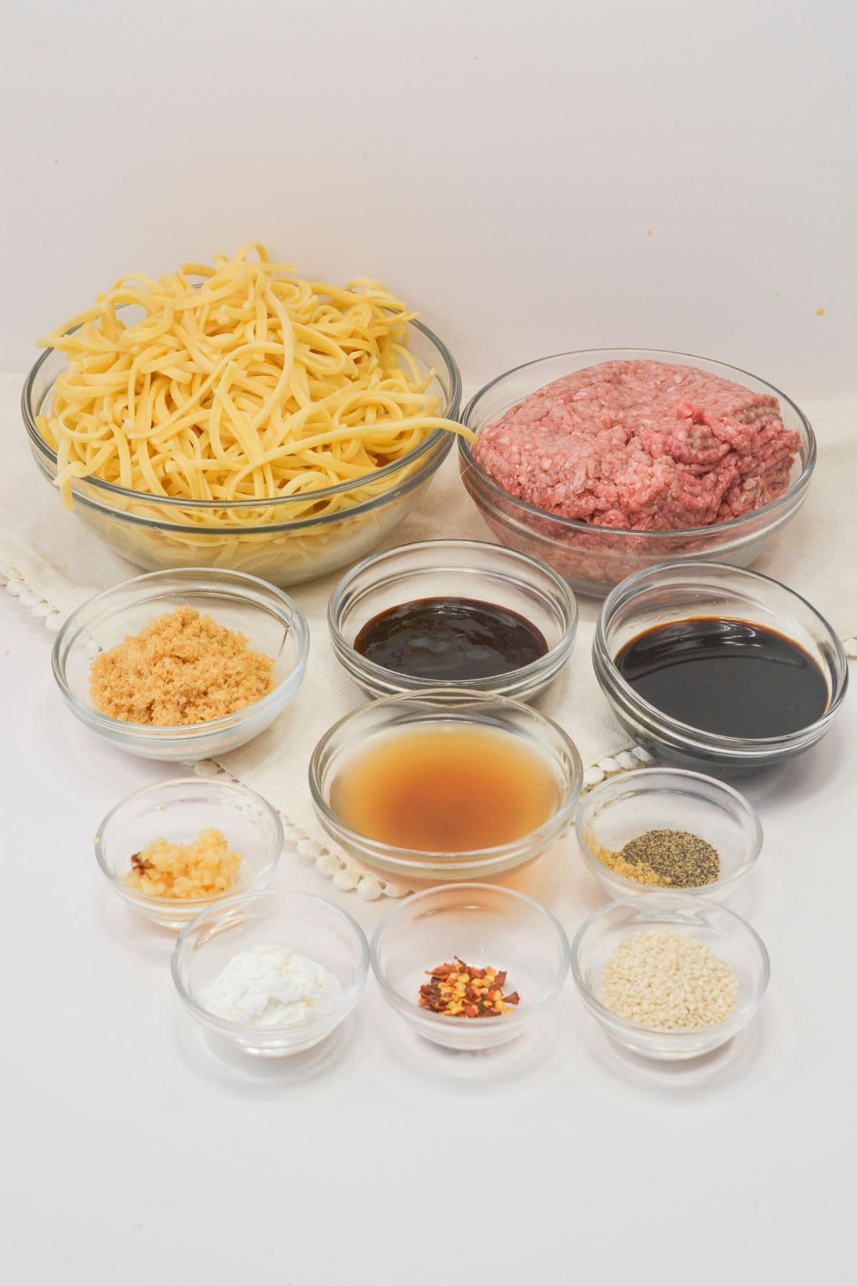 Clear glass dishes with the ground meat, pasta and sauce ingredients.