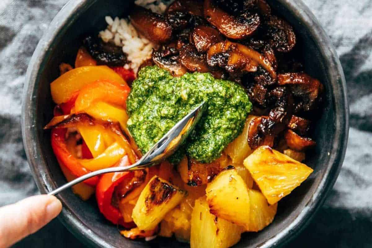 A must try bowl of rice topped with sautéed mushrooms, grilled pineapple, sliced bell peppers, and a dollop of green sauce takes mushroom dishes beyond the basics—a spoon resting on top completes the experience.
