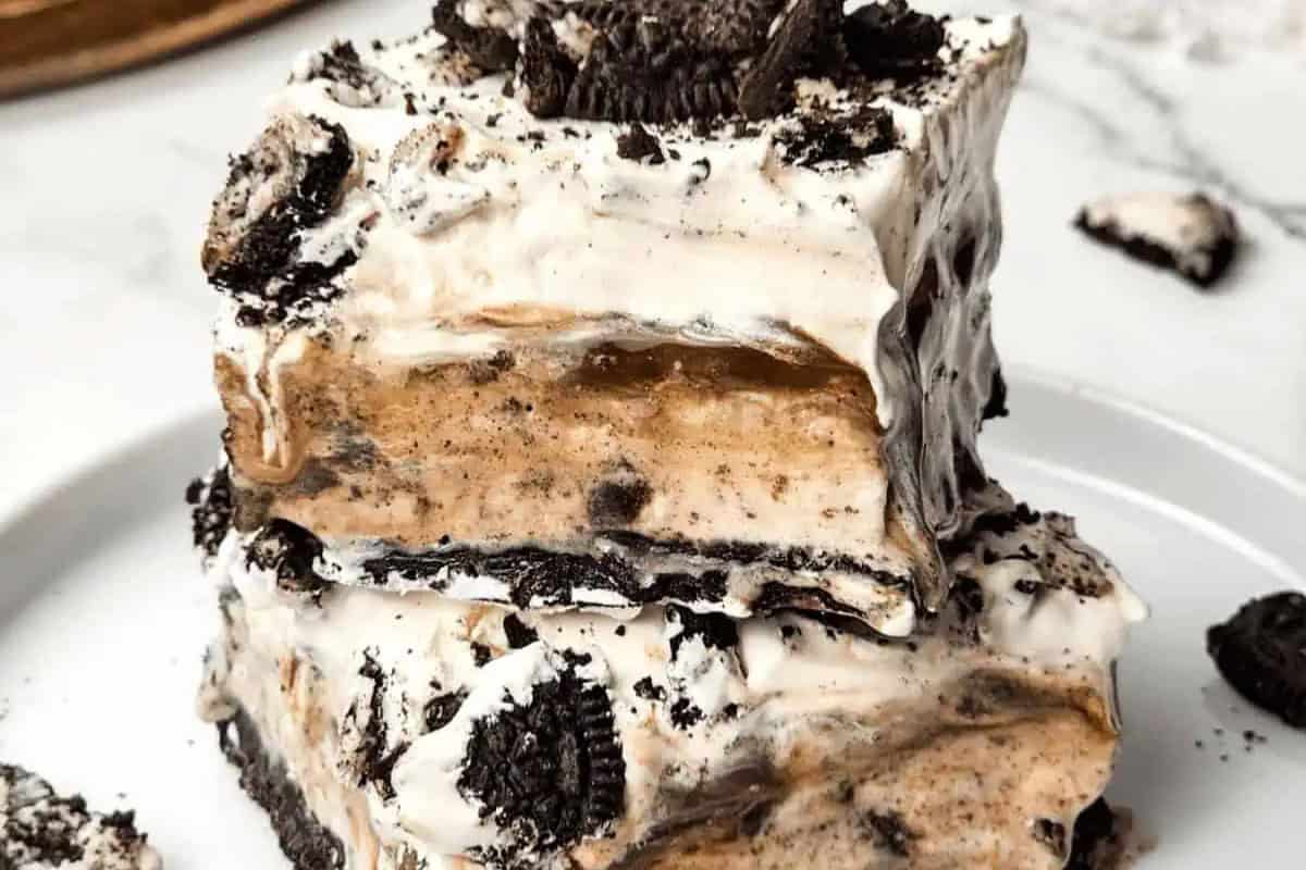 A close-up of two stacked slices of cookies and cream dessert with layers of whipped cream, chocolate cookies, and a creamy filling on a white plate—a perfect choice for lovers of irresistible frozen desserts.